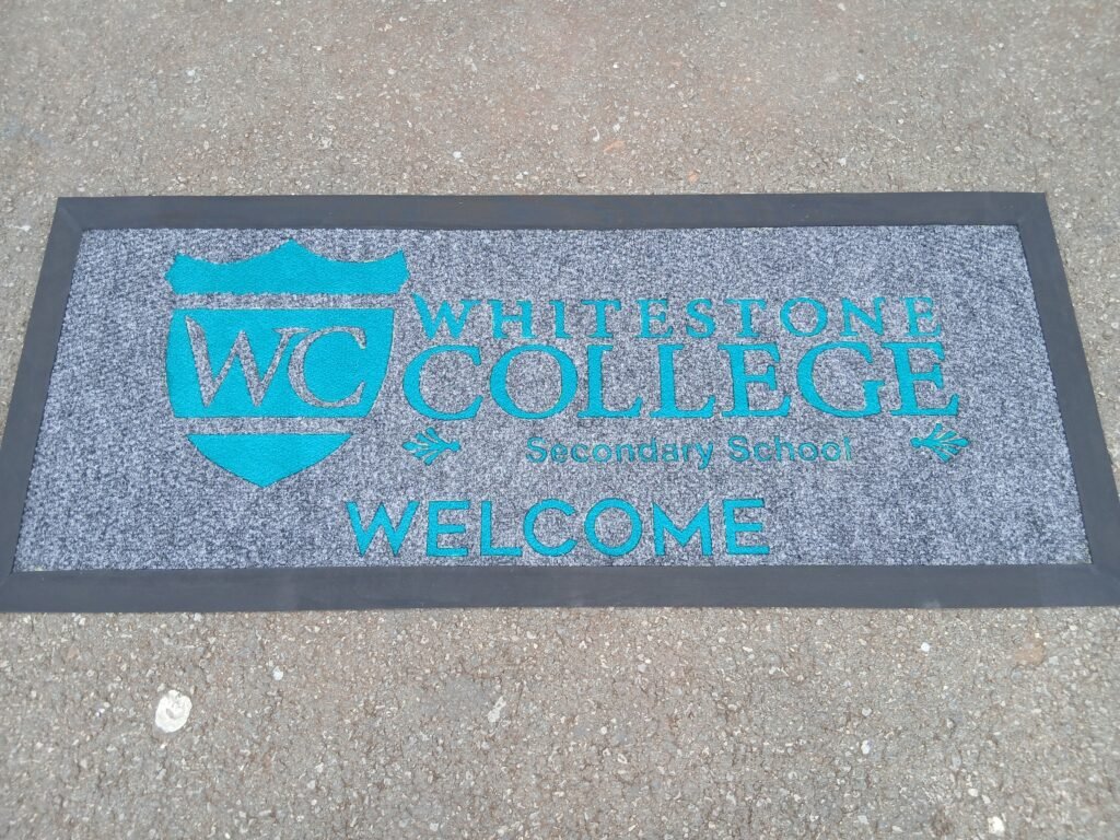 Whitestone College welcome mat with turquoise lettering on grey carpet and black edging
