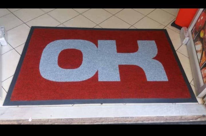Red and grey OK logo mat with black edging fitted inside a tiled shop entrance
